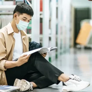 Student reading book in library wearing mask